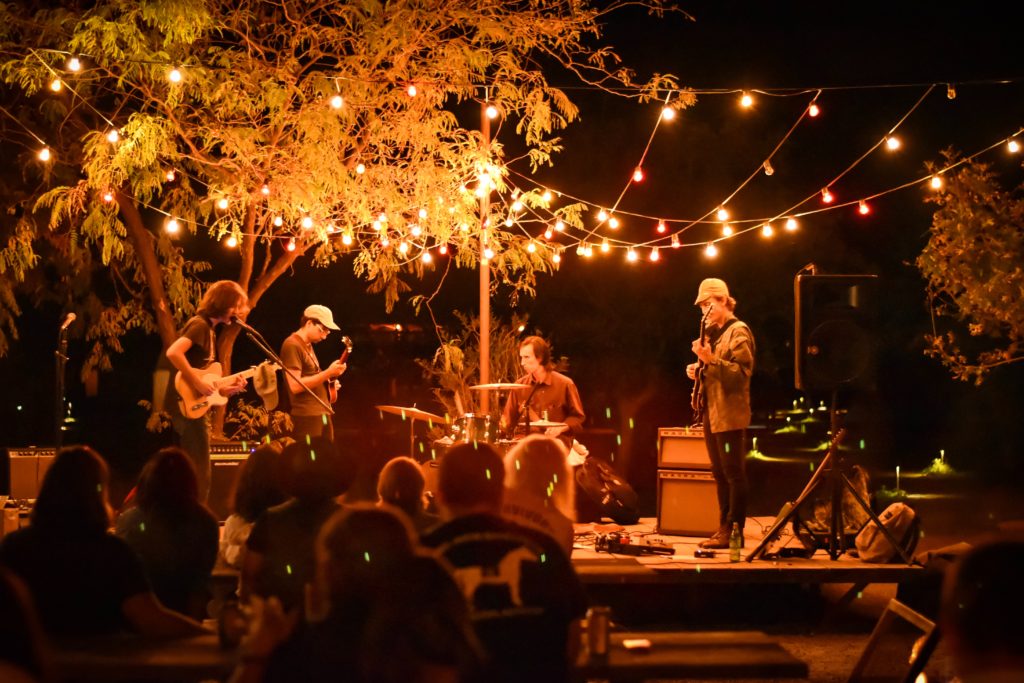 A live band performing for an audience under string lights at El Cosmico. 