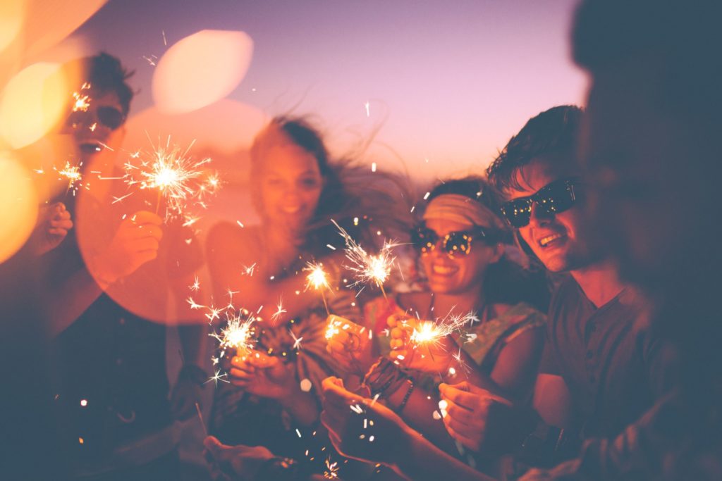 Group of friends having a beach party together and celebrating with sparklers in the  twilight