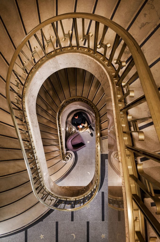 Aerial view of man sitting in a chair at the bottom of a gold spiral staircase at Rand Tower Hotel