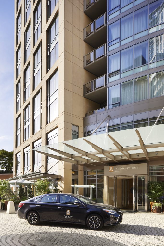 Front entrance of Pan Pacific Seattle hotel with black luxury car parked in front.