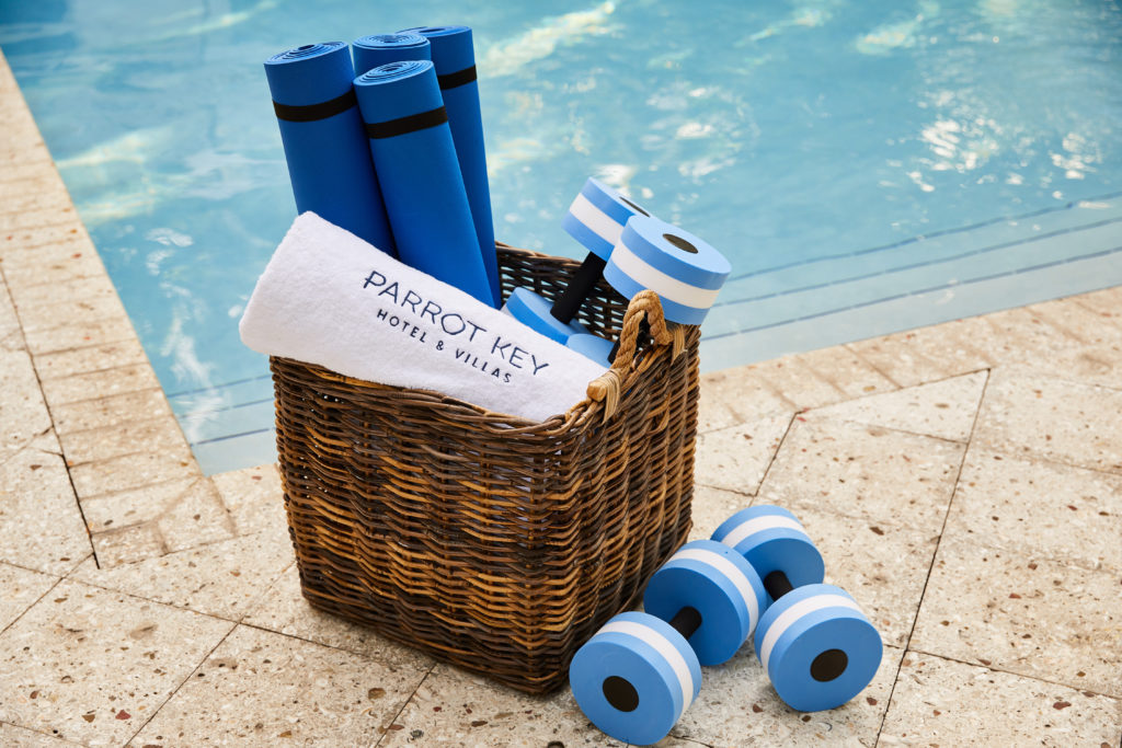 Basket of exercise equipment by the pool at Parrot Key Hotel & Villas. Includes weights, yoga mats, and towels.
