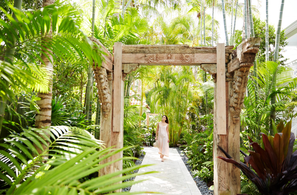woman walking toward wooden hand carved arch on lush tropical foliage surrounded path at Parrot Key Hotel & Villas