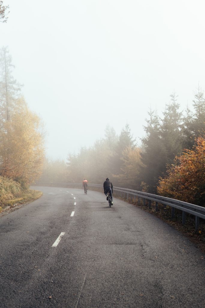 Two people bicycling on a road in the fog during autumn