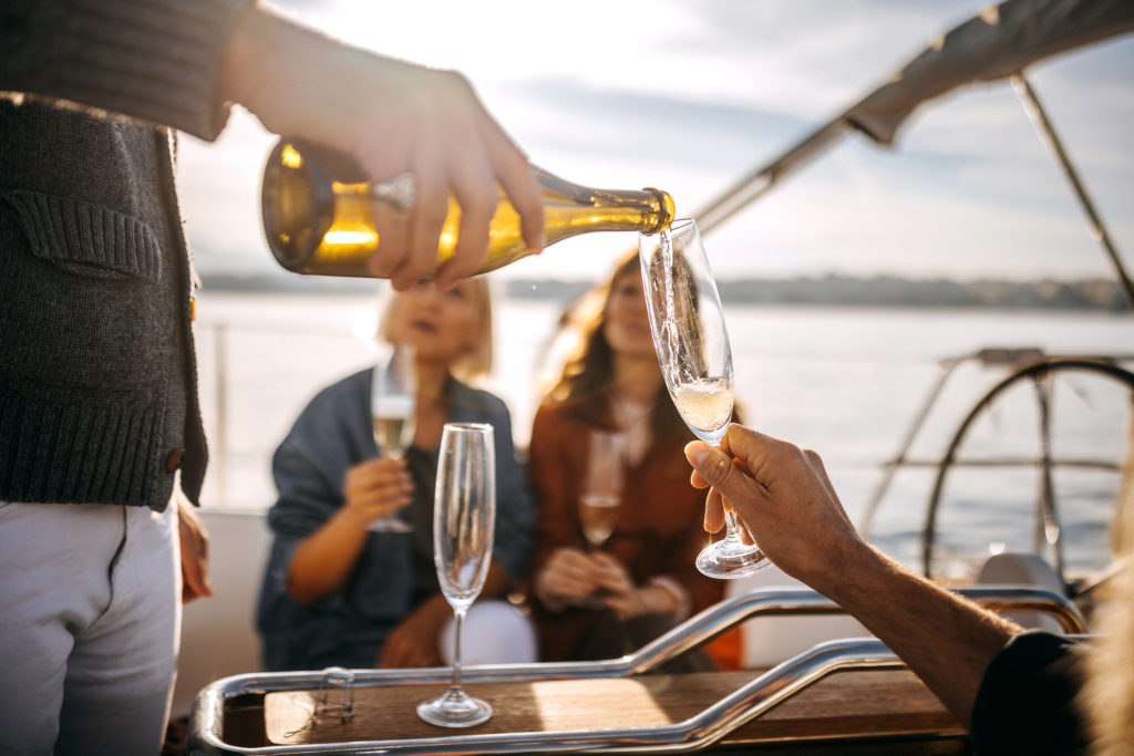 Close up of well dressed man pouring champagne while on yacht with his friends