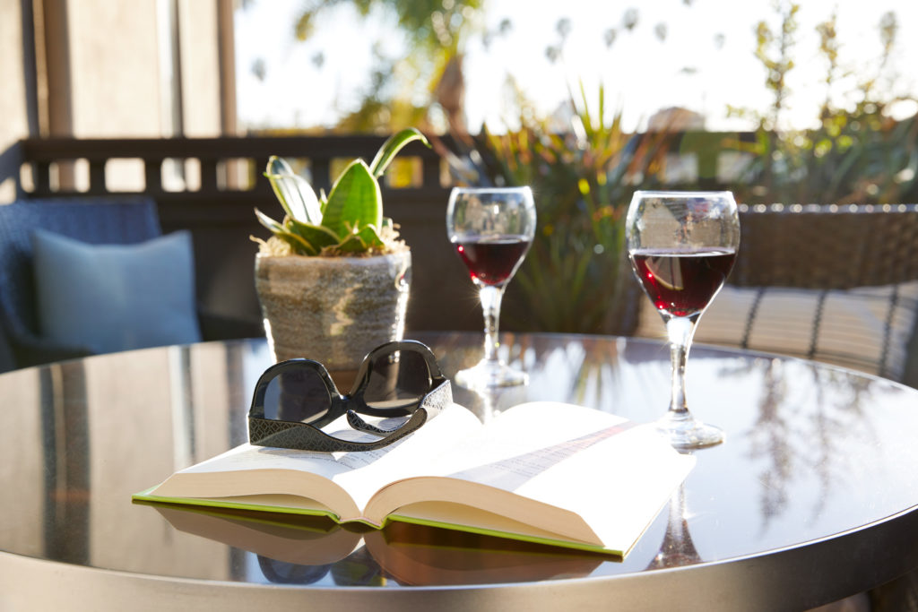 A book, sunglasses, and two glasses of wine on a patio table at The Ambrose Hotel in Santa Monica