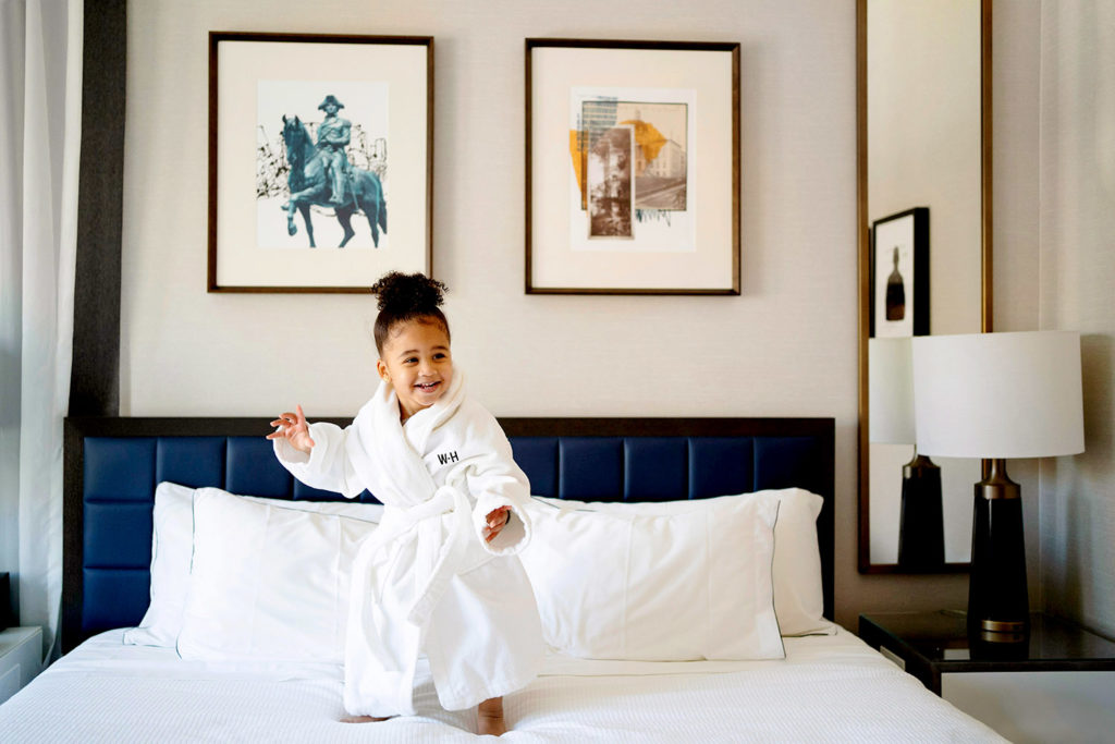 Little girl wearing a hotel robe standing on a bed at The Whitney Hotel Boston
